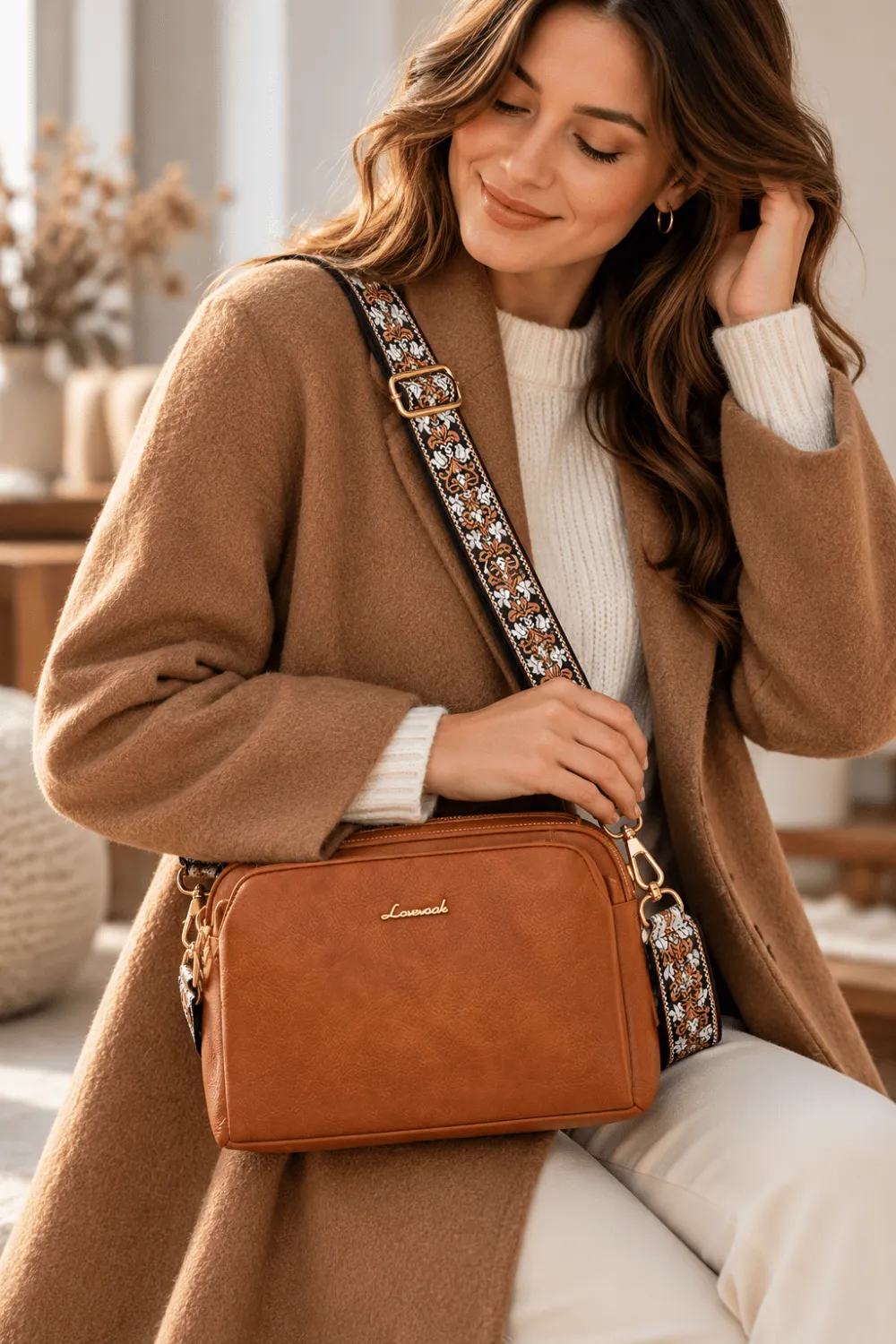Woman styling a brown crossbody bag with a patterned shoulder strap over a camel cardigan and cream outfit.